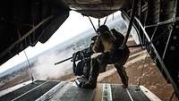 Ein Soldat steht auf der Heckklappe eine Helikopters und schiesst mit einem Maschinengewehr