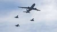 Ein Tankflugzeug, zwei Eurofighter und ein Tornado fliegen in Formation vor blau-weißem Himmel. 