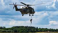 Ein Soldat hängt an einem Seil unter einem Hubschrauber und gleitet zum Boden. 