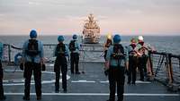 Mehrere Soldaten schauen am Deck auf ein anderes Schiff