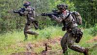 Soldaten stürmen mit ihren Waffen im Anschlag durch den Wald.