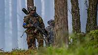 Bewaffnete Infanteristen laufen durch den Wald.