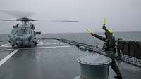 Der Flugdeckoffizier weist einen Bordhelikopter ein, der gerade auf dem Flugdeck aufsetzt