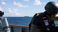 Ein amerikanisches Schiff wird eskortiert und ist im Hintergrund eines Soldaten zu sehen