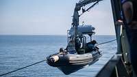 Ein Speedboot mit Soldaten an Bord wird an einem Kranausleger hängend zu Wasser gelassen