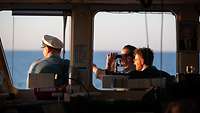 Drei Soldaten schauen auf dem Außendeck vor der Brücke aufs Meer, einer benutzt dafür ein Fernglas