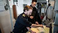 Two soldiers on board a ship are drawing something on a map with a compass.