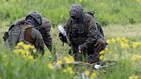 Drei Soldaten versorgen bei der NATO-Übung Vigorous Warrior in Estland einen Verwundeten auf einer Wiese.