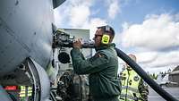 Soldat der Bundeswehr schließt einen Tankschlauch an die Tankkupplung eines Militärflugzeuges an.
