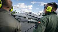 Kampfflugzeug F/A-18 der finnischen Luftstreitkräfte. Im Vordergrund zwei Soldaten der Bundeswehr.