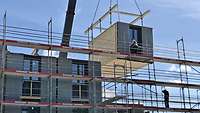 Ein Gebäude, wird aus vorgefertigten Modulen zusammengesetzt. Ein Modul wird mit einem Kran montiert.