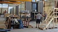Drei Männer in einer großen Werkstatthalle verkleiden die gefertigten Holzmodule.