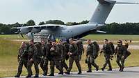 Soldaten mit Gepäck marschieren vor einem A400M-Transportflugzeug.