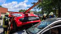 Ein Auto ist mit einem Rotorblatt durchbohrt. Drei Feuerwehrmänner helfen.
