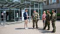Fünf Personen, militärisch und zivil, stehen vor einem Krankenhaus und sprechen miteinander.