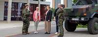 Fünf Personen, militärisch und zivil, stehen vor einem Gebäude. Rechts im Bild steht ein militärisches Fahrzeug.