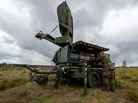 Ein Anhänger mit Satellitenschüssel darauf. An einer angebauten Bedienerkonsole steht ein Soldat.