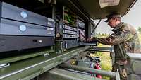 Der Bediener der SatCom-Anlage steht an seinem Laptop, der mit der Technik der Anlage verbunden ist.
