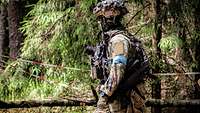 Ein Soldat des Forward Media Teams mit Kamera und Waffe im Wald.
