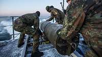 Drei Soldaten schieben eine Grundmine von Bord eines Minenjagdbootes ins Wasser.