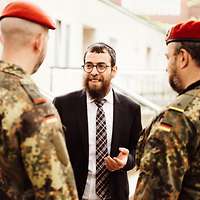 Ein Rabbiner mit Kippa ist von Soldaten umringt.