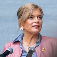 blonde Frau in blauem Kleid und rosa Jacke am Rednerpult