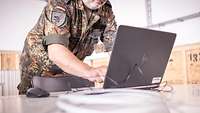Ein Soldat steht vor einem Laptop und tippt etwas ein.