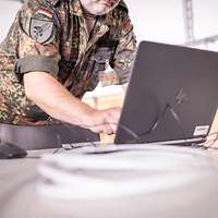 Ein Soldat steht vor einem Laptop und tippt etwas ein.