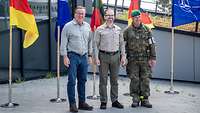 Drei Männer stehen nebeneinander vor deutschen, litauischen und NATO-Flaggen.