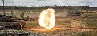 Kampfpanzer bei der Schussabgabe mit Feuerball und sichtbarem Projektil.