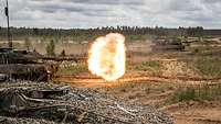 Kampfpanzer bei der Schussabgabe mit Feuerball und sichtbarem Projektil.