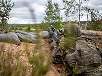 Ein Soldat mit Waffe in einer Mulde im Waldboden.