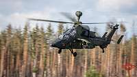 Ein Kampfhubschrauber fliegt vor Bäumen.