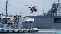 Ein Soldat seilt sich von einem Hubschrauber auf einen im Hafen liegenden Hafenschlepper ab.