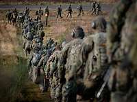 Viele Soldaten marschieren in Reihe über einen Truppenübungsplatz während einer Übung.
