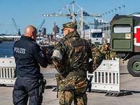 Ein Soldat und ein Polizist stehen nebeneinander vor einer Absperrung im Hafen während einer Übung.