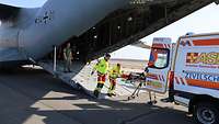 ASB-Mitarbeiter rollen einen Patienten aus einem Militärflugzeug zum Rettungswagen bei einer Übung.