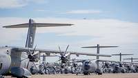 Auf dem Fliegerhorst Wunstorf stehen viele A400M. Darüber ist ein A400M im Steigflug nach dem Start.