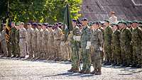 Deutsche und niederländische Soldaten stehen angetreten nebeneinander, ein Soldat hält eine Flagge