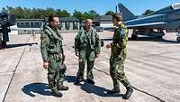 Drei Soldaten stehen vor einem Kampfjet. Sie unterhalten sich und lächeln.