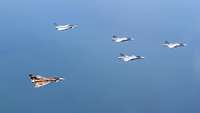 Fünf Flugzeuge fliegen in einer Formation über dem Meer.