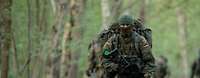 Ein Soldat in vollständiger Ausrüstung und mit verdecktem Gesicht läuft durch einen Wald