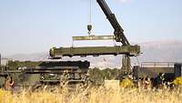 Ein Bundeswehrkran bewegt einen Lenkflugkörper von einem LKW auf das Flugabwehrsystems Patriot