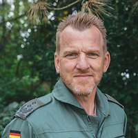 Ein Soldat lächelt vor einem Busch