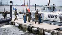 Bewaffnete Soldaten steigen aus einem Schlauchboot aus und laufen einen Bootssteg entlang.