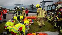 Feuerwehrleute und Soldaten versorgen Verletzte bei einer Unfallübung. Im Hintergrund steht ein A400M. 