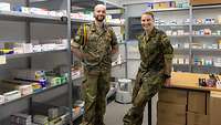 Soldat und Soldatin in einem Raum mit Regalen voller Medikamente.