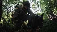 Ein Soldat kniet im Wald und arbeitet an einem schwarzen Koffer.