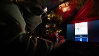 Ein Soldat liegt in einem Versteck vor einem Laptop und schreibt etwas auf.