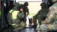 Ein Hund springt in einen Hubschrauber, darin bereits mehrere Soldaten